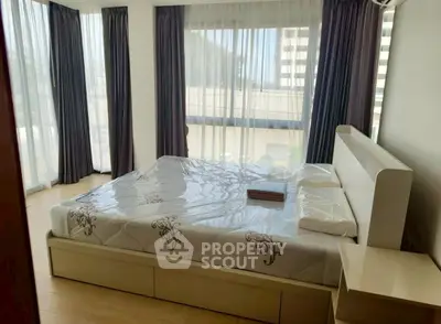 Spacious bedroom with large windows and modern furnishings in a high-rise apartment.
