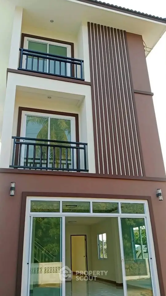 Modern three-story townhouse with large windows and balconies, showcasing contemporary architectural design.