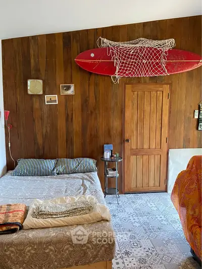 Cozy bedroom with rustic wooden wall and surfboard decor, perfect for beach lovers.