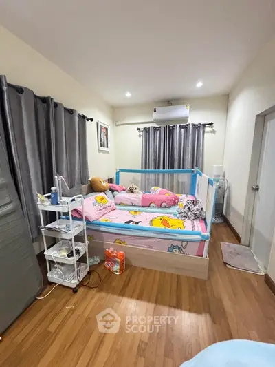 Cozy bedroom with wooden flooring and playful decor, featuring a comfortable bed and ample natural light.