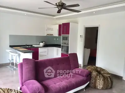 Modern open-layout living room with vibrant purple sofa and sleek kitchen area.