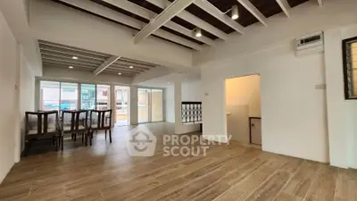 Spacious open-plan living area with wooden flooring and dining set, featuring large windows for natural light.