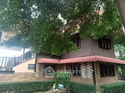 Charming two-story home nestled under lush greenery with a unique brick facade and cozy design, featuring a shaded porch and tranquil surroundings.