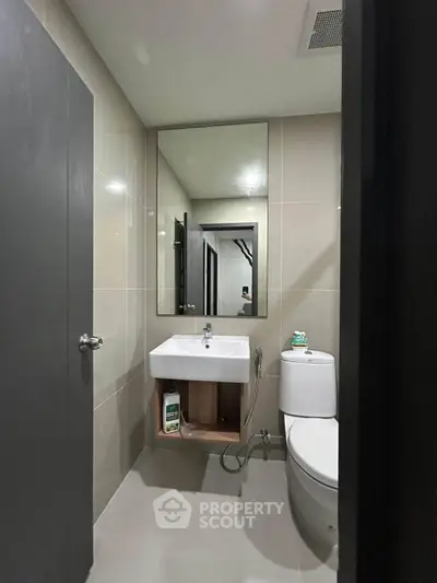 Modern bathroom with sleek fixtures and neutral tones, featuring a large mirror and compact design.