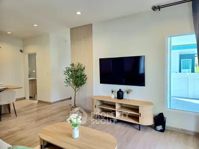 Modern living room with stylish decor and large TV, featuring natural light and elegant furnishings.