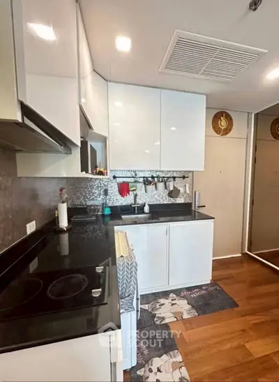 Modern kitchen with sleek white cabinets and black countertops, featuring a stylish backsplash and wooden flooring.