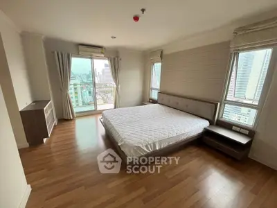 Spacious bedroom with city view, featuring large windows and modern furnishings in a high-rise apartment.