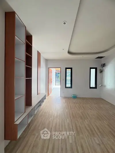 Spacious modern living room with wooden flooring and built-in shelves, ample natural light.