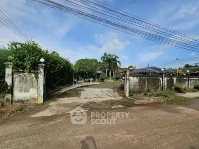 Spacious property entrance with lush greenery and clear blue sky.