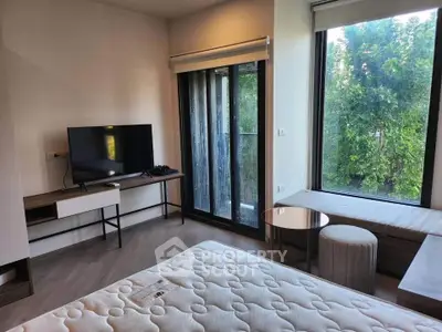 Modern bedroom with large windows and natural light, featuring a TV and stylish furniture.