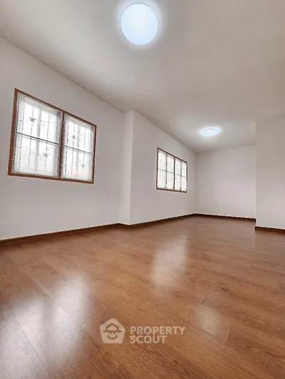 Spacious and well-lit empty room with polished hardwood floors and multiple windows offering ample natural light, ideal for a customizable living space.