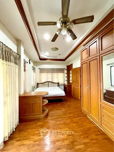 Spacious bedroom with wooden flooring and built-in wardrobe, featuring a ceiling fan and large windows.