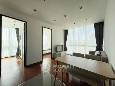 Modern living room with large windows and city view, featuring a cozy sofa and dining table.