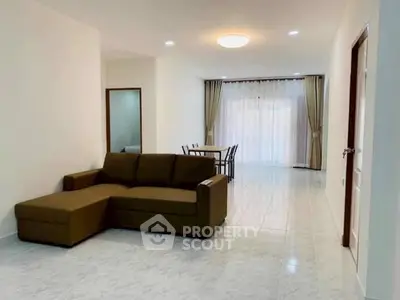 Spacious living room with brown sectional sofa and dining area, featuring large windows and elegant curtains.