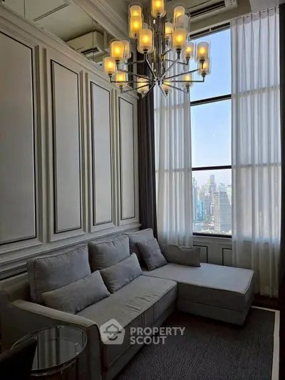 Elegant living room with high ceilings and city view, featuring a modern chandelier and cozy gray sofa.