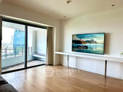 Spacious living room with large balcony and modern TV setup in urban apartment.