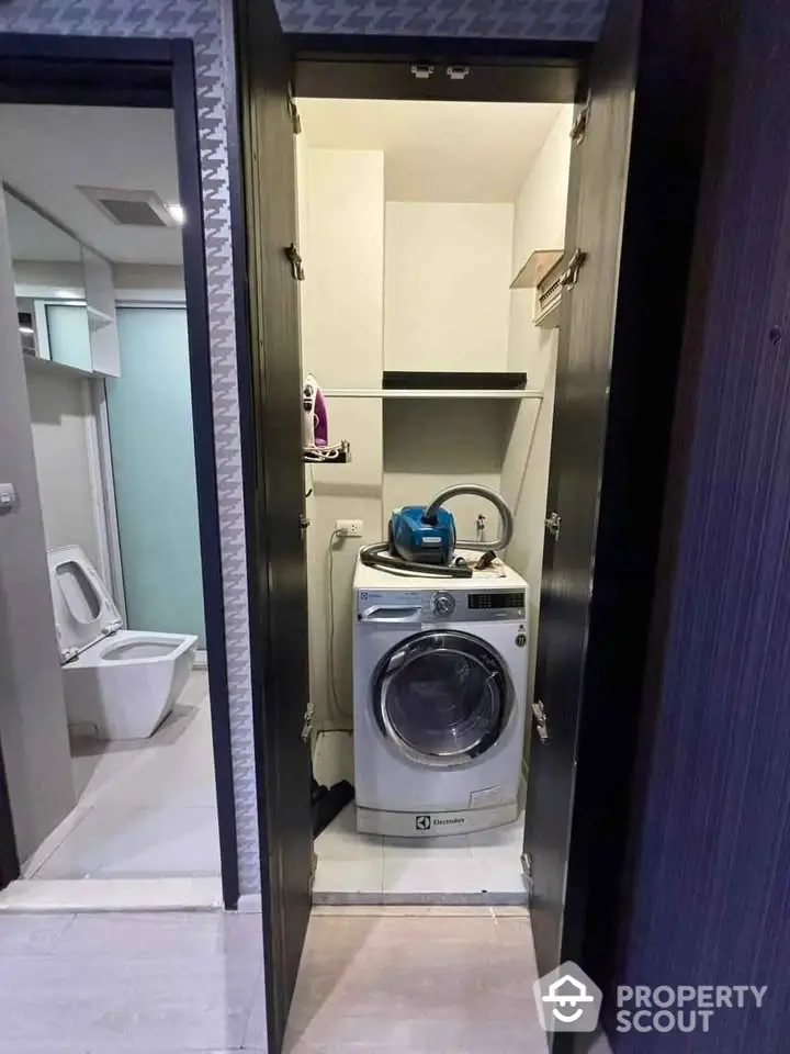 Compact laundry area with modern washing machine and storage shelves in a stylish apartment.