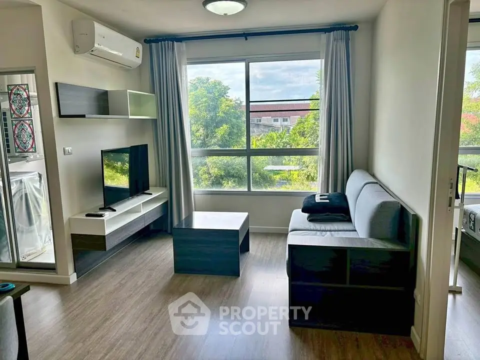 Modern living room with large window and stylish furniture, offering a serene view of lush greenery.