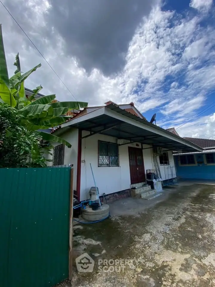 Charming single-story home with lush greenery and spacious driveway under a dramatic sky.