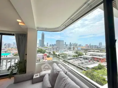 Spacious living room with panoramic city view through large corner windows, featuring modern sofa and bright ambiance.