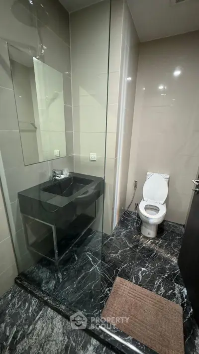 Modern bathroom with sleek black marble flooring and glass shower enclosure.