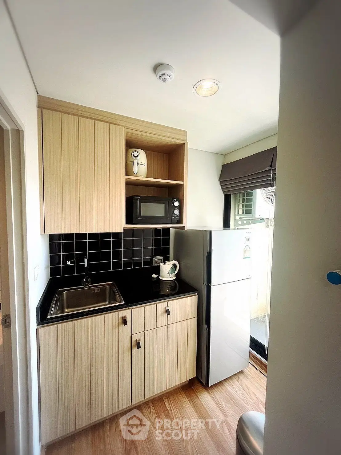 Modern compact kitchen with wooden cabinets, black countertop, and stainless steel appliances in cozy apartment.