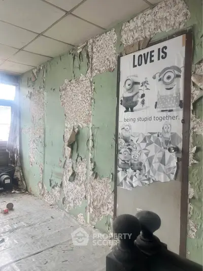 Fixer-upper room with peeling walls and humorous poster, ideal for renovation enthusiasts.