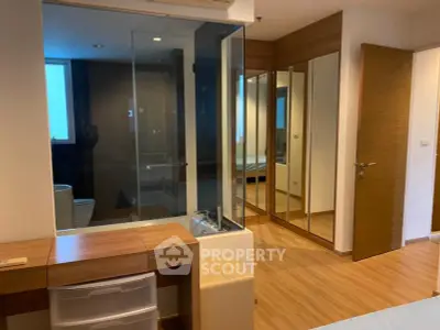 Spacious bedroom with modern design and glass partitioned bathroom, featuring wooden flooring and mirrored wardrobe.