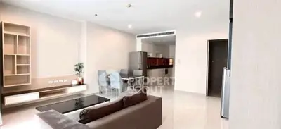 Spacious modern living room with open kitchen and dining area, featuring sleek furniture and bright lighting.