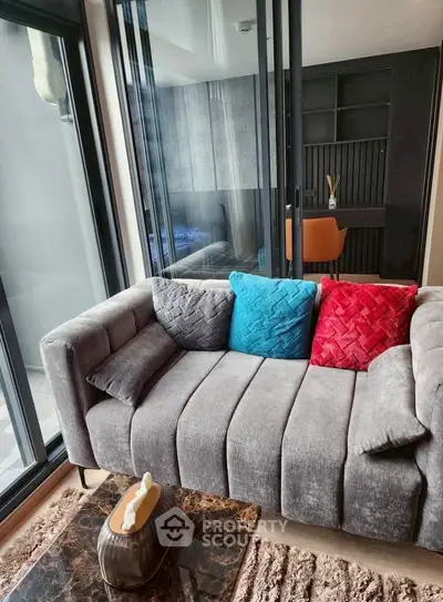 Modern living room with stylish sofa and vibrant cushions, featuring floor-to-ceiling windows and sleek decor.