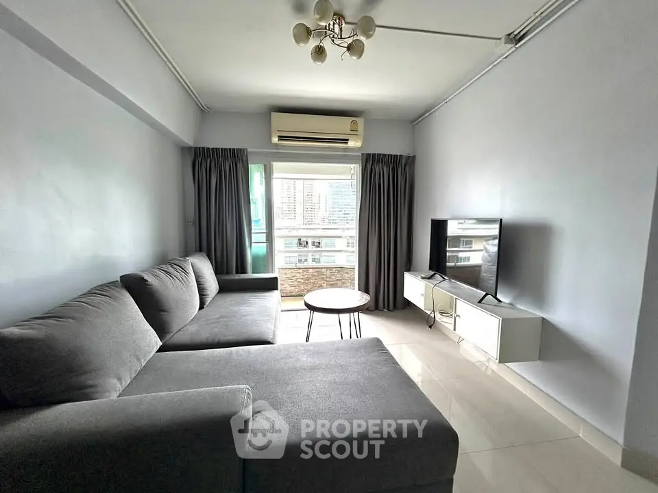 Spacious living room with modern gray sofa and large window offering city views.