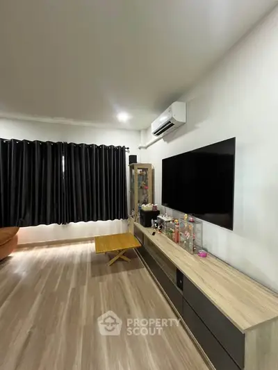 Modern living room with sleek TV setup and air conditioning, featuring stylish wooden flooring and elegant curtains.