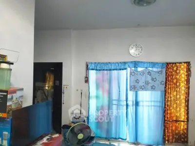 Cozy living room with blue curtains and wall clock, featuring a fan and TV setup.