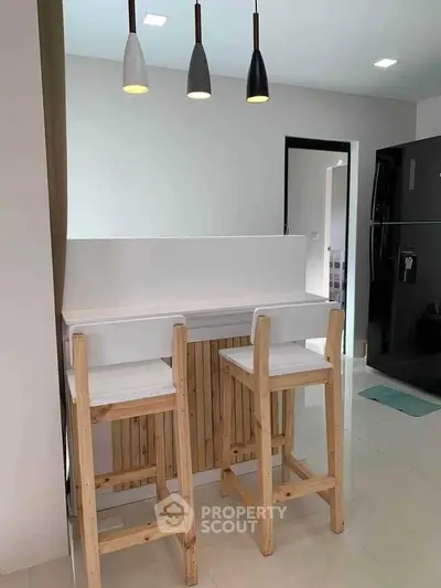 Modern kitchen with bar stools and pendant lighting in sleek apartment.