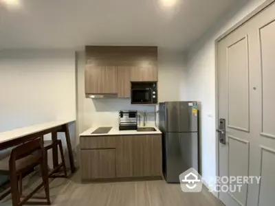 Modern compact kitchen with sleek wooden cabinets and stainless steel appliances in a stylish apartment.