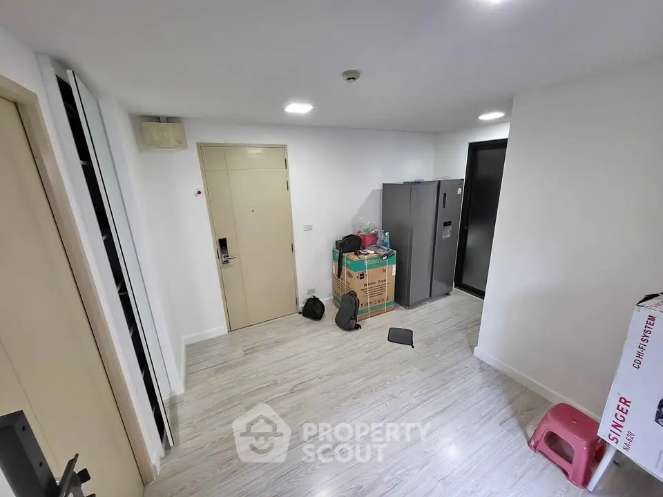 Compact apartment entryway with light wood flooring and modern appliances.