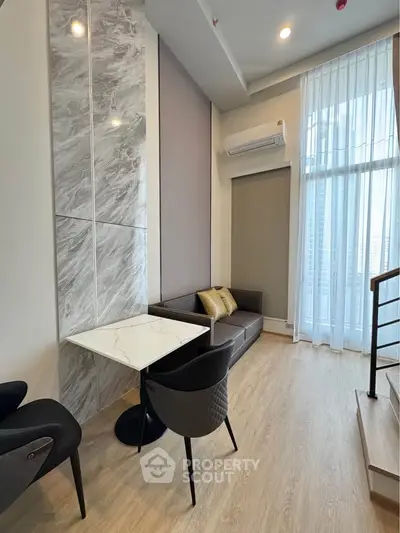 Modern living room with high ceiling, elegant furniture, and large windows for natural light.