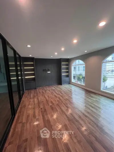Spacious modern living room with wooden flooring and large windows offering natural light.