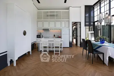 Modern kitchen with open layout and stylish dining area, featuring elegant wood flooring and large windows.