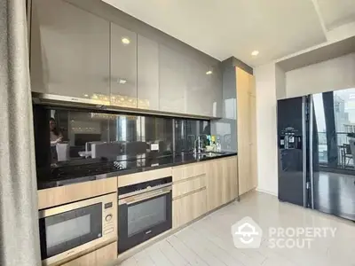 Sleek modern kitchen with high-end built-in appliances, ample cabinetry, and a spacious open layout leading to a sunlit balcony.