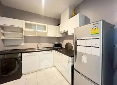 Modern kitchen with sleek white cabinets, stainless steel fridge, and washing machine.