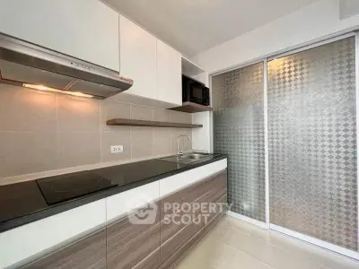 Modern kitchen with sleek cabinetry and electric cooktop in a contemporary apartment.