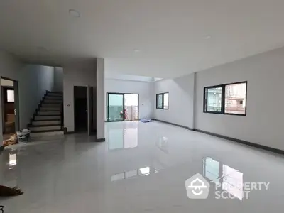 Spacious and bright unfurnished living room with glossy tiled floors, large windows, and an elegant staircase leading to the upper level.