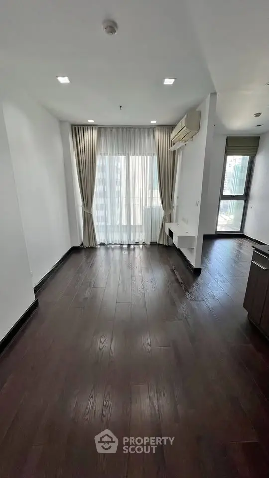 Spacious living room with dark wood flooring and large windows offering city views.