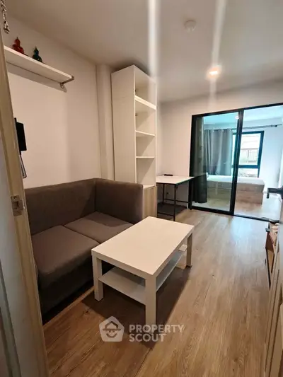 Modern living room with cozy sofa and sliding glass doors leading to a bedroom, featuring wooden flooring.