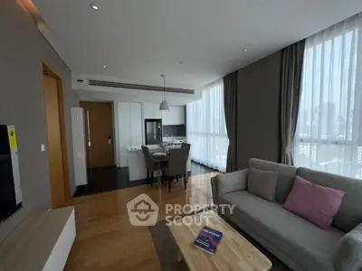 Modern living room with open kitchen, featuring sleek furniture and large windows for natural light.