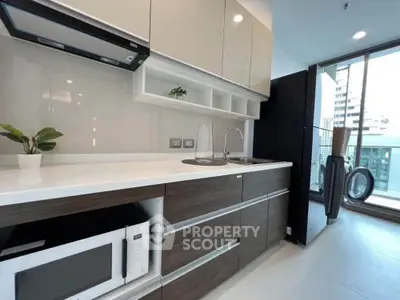 Modern kitchen with sleek cabinetry and appliances, featuring a microwave and washing machine, in a bright apartment.