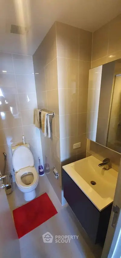 Modern bathroom with sleek fixtures and red mat, featuring a compact design and elegant tiling.