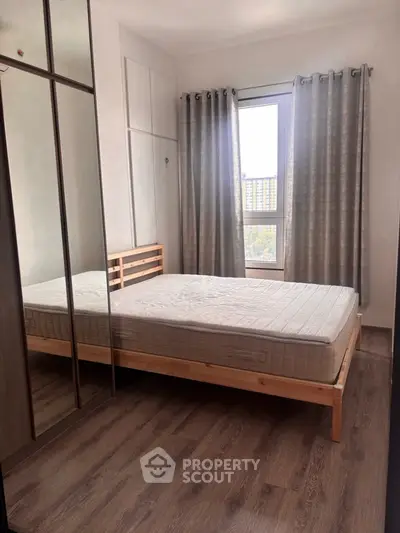 Cozy bedroom with wooden flooring and large window offering natural light.