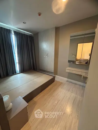 Modern bedroom with wooden flooring and large window, featuring a built-in bed frame and sleek vanity mirror.